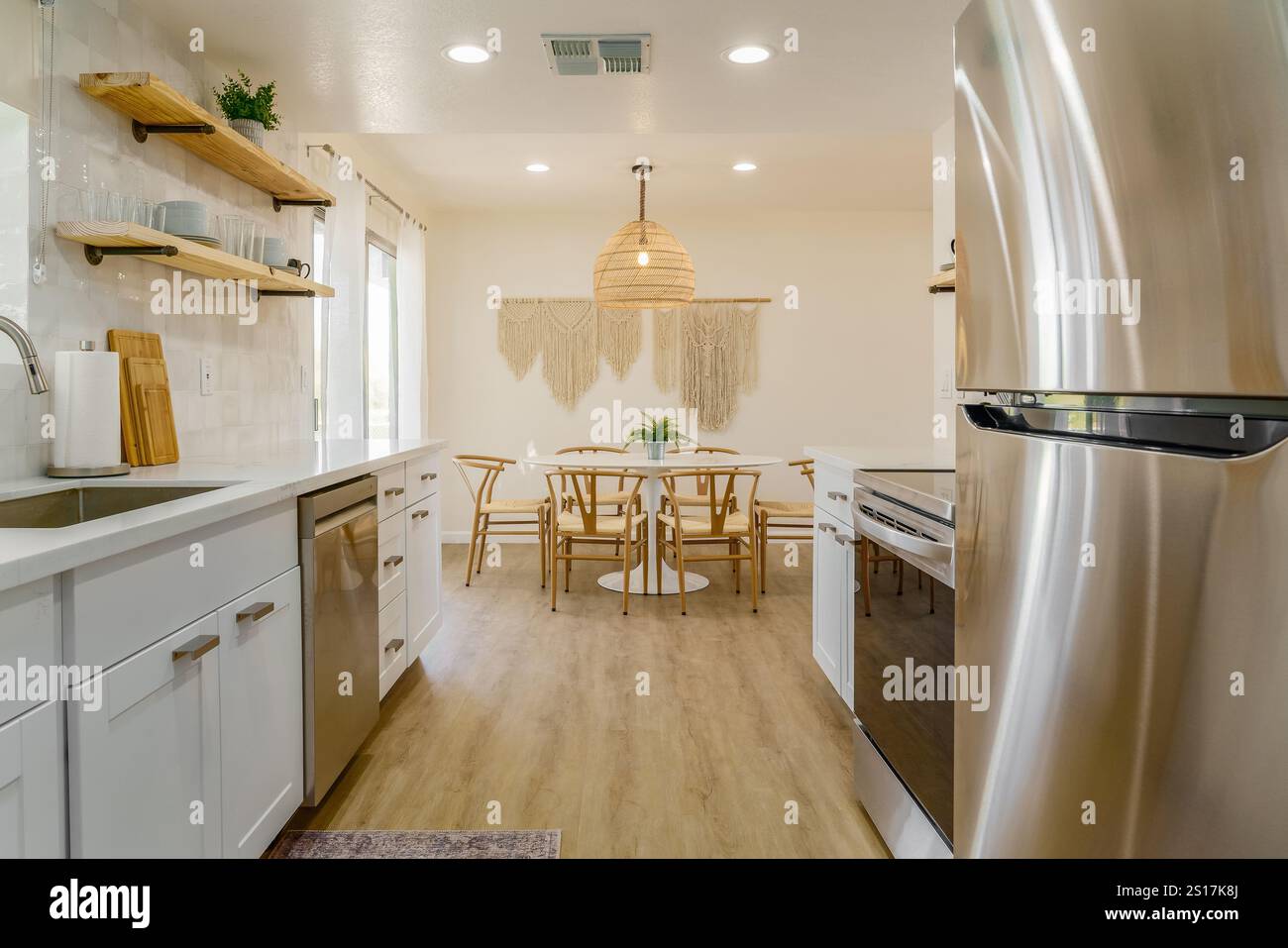 Cuisine moderne avec armoires blanches, appareils en acier inoxydable et table à manger. Banque D'Images