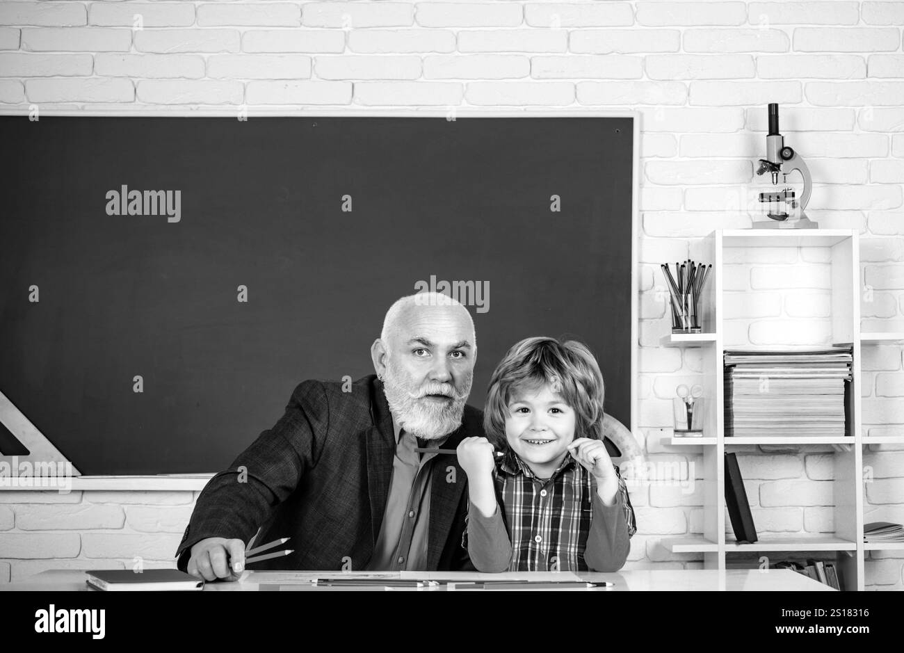 Grand-père et fils s'amusant ensemble. Heureux petit-fils et grand-père assis à un bureau à l'intérieur. Retour à l'école. Concept d'apprentissage et d'éducation Banque D'Images