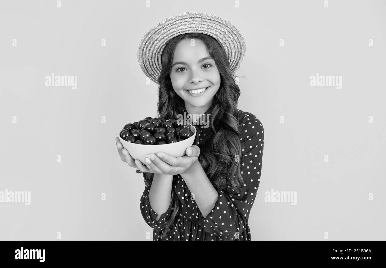 un enfant heureux tient un bol de cerise sur fond jaune. Banque D'Images