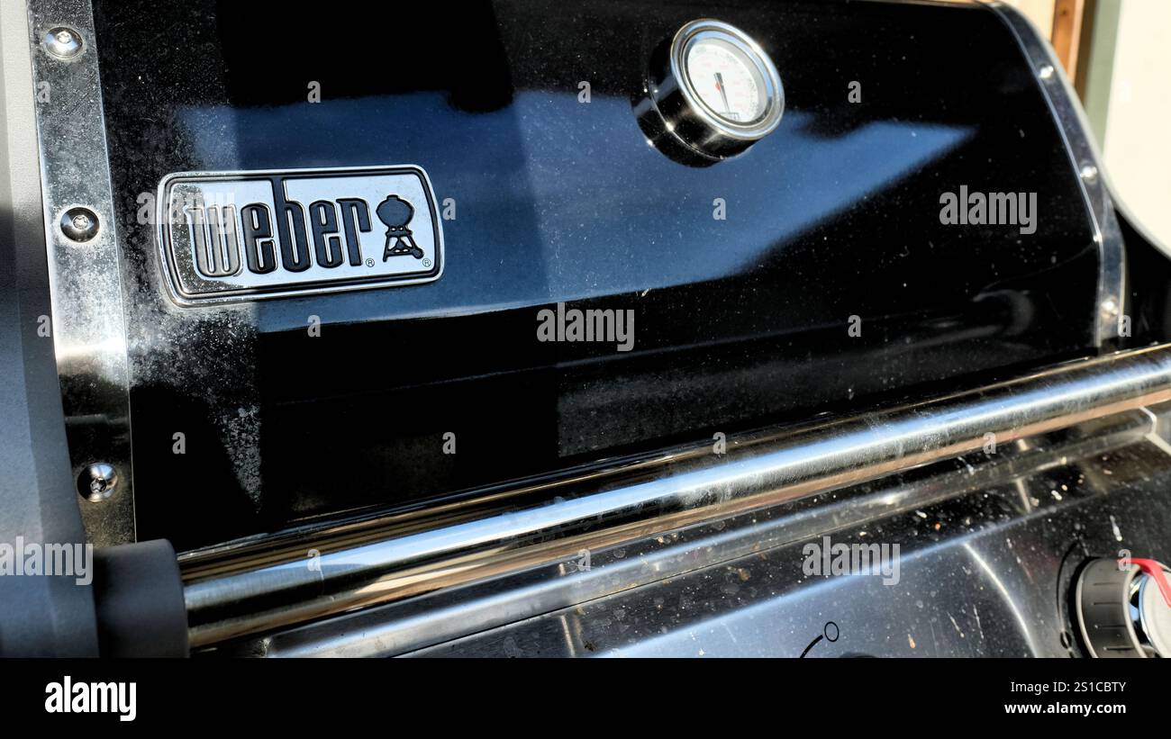 Couvercle de gril extérieur de marque Weber avec lecture de la jauge de température en degrés Celsius et Fahrenheit ; émail noir avec des taches d'eau sale après la pluie. Banque D'Images