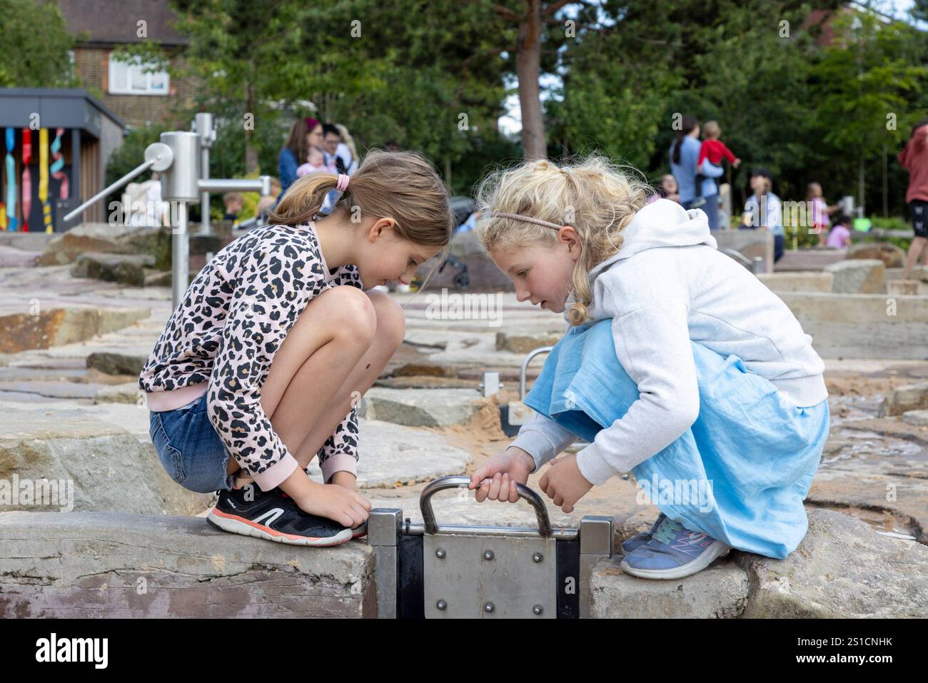 Deux sœurs, 8 et 7 jouent avec un jeu d'eau dans une aire de jeux à Brent Cross Town, un développement dans le nord-ouest de Londres Banque D'Images