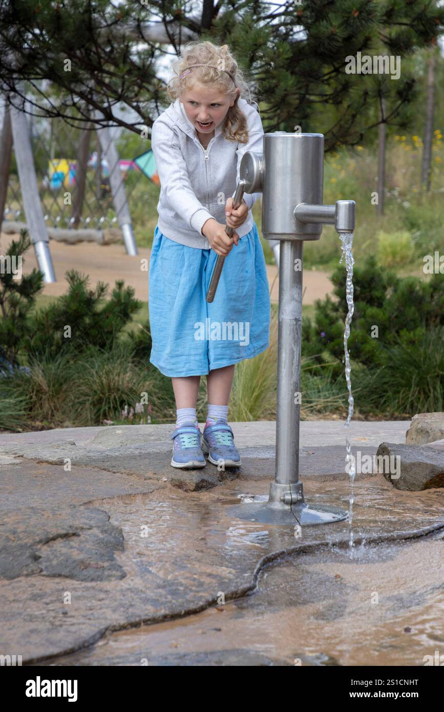 Une jeune fille de 7 ans joue avec une pompe à eau dans une aire de jeux à Brent Cross Town, un développement dans le nord-ouest de Londres Banque D'Images