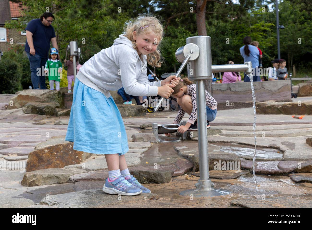 Une jeune fille de 7 ans joue avec une pompe à eau dans une aire de jeux à Brent Cross Town, un développement dans le nord-ouest de Londres Banque D'Images