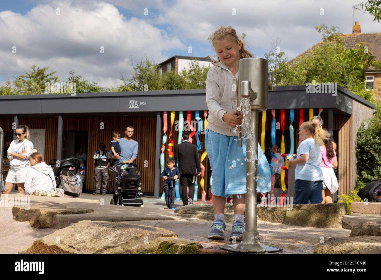 Une jeune fille de 7 ans joue avec une pompe à eau dans une aire de jeux à Brent Cross Town, un développement dans le nord-ouest de Londres Banque D'Images