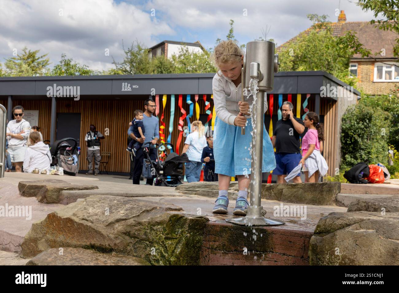 Une jeune fille de 7 ans joue avec une pompe à eau dans une aire de jeux à Brent Cross Town, un développement dans le nord-ouest de Londres Banque D'Images