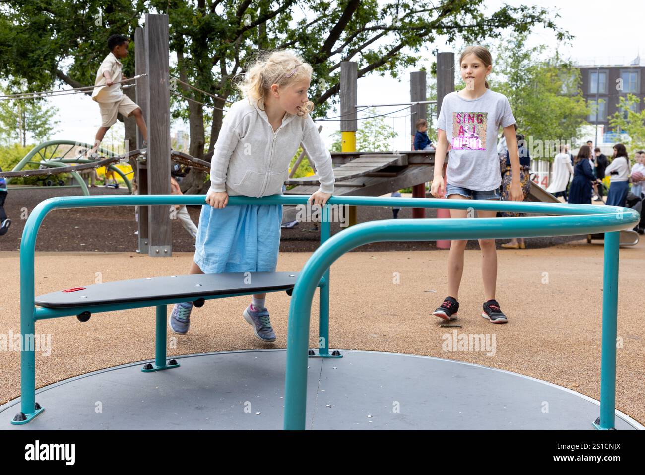 Une jeune fille blanche de 7 ans tourne sur un rond-point dans une aire de jeux à Brent Cross Town, un développement dans le nord-ouest de Londres. Sa sœur de 8 ans est derrière elle. Banque D'Images