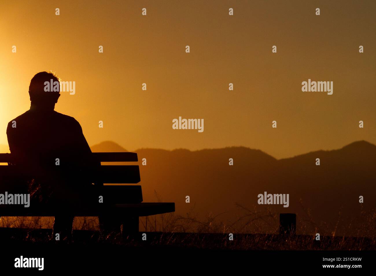 Un homme assis sur un banc regardant le coucher du soleil depuis le parc Oyamada ryokuchi, Machida, Tokyo, Japon. Banque D'Images