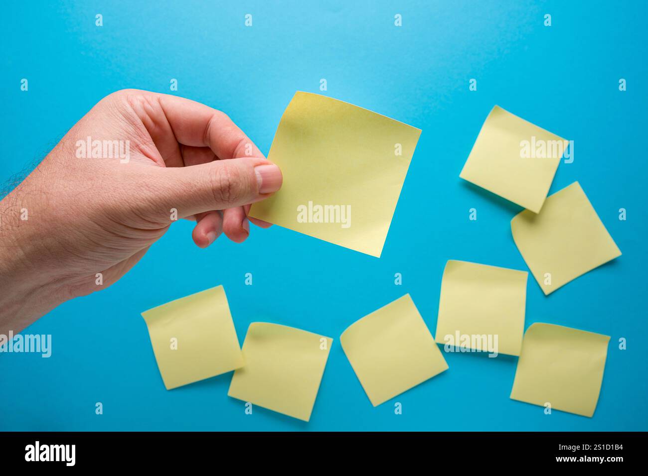 Une main tient une note adhésive jaune vierge sur fond bleu et des notes adhésives floues reposent sur le sol Banque D'Images