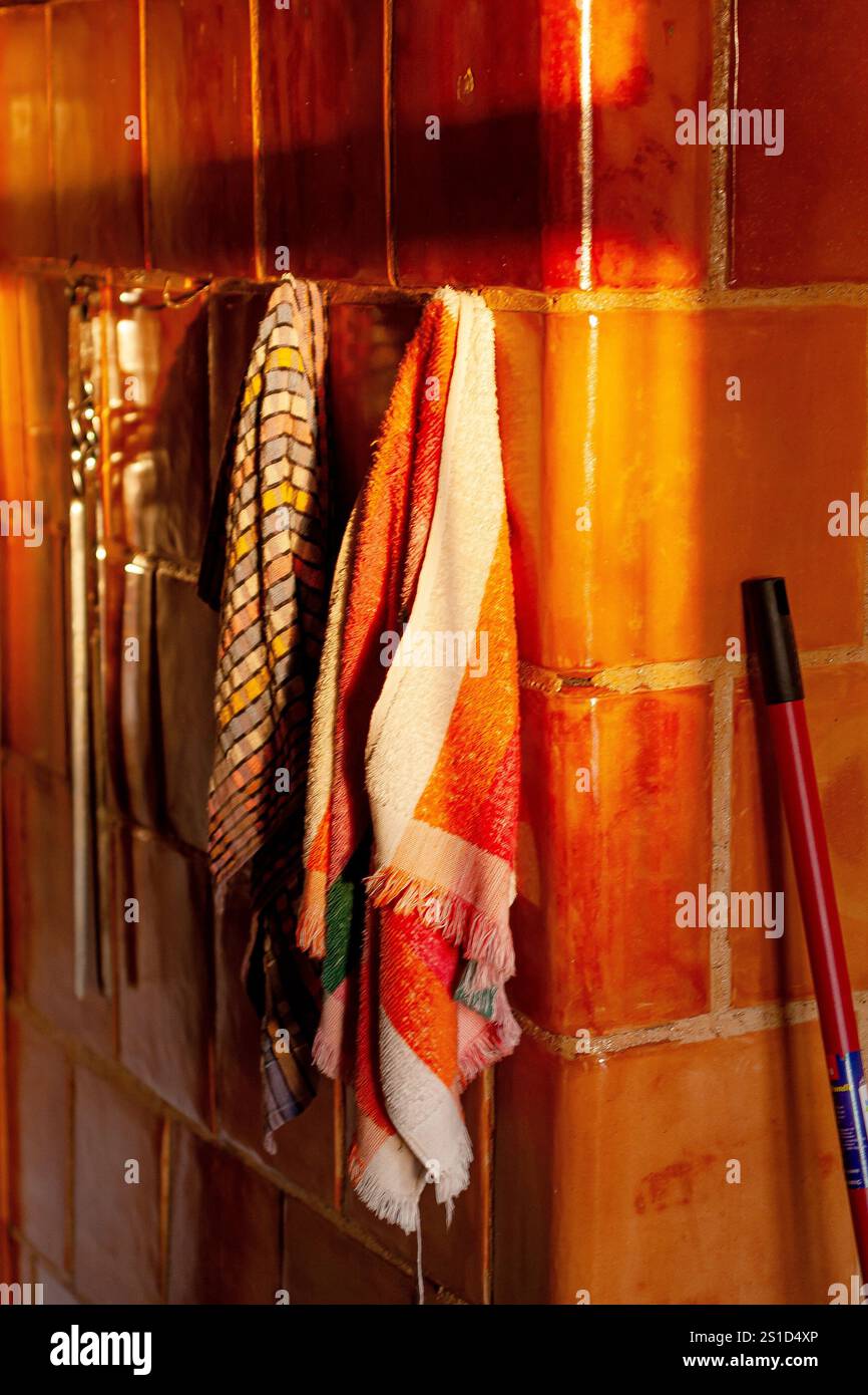 Scène ensoleillée avec des serviettes de cuisine vibrantes suspendues sur un mur de carreaux de céramique chaud ajoutant une chaleur visuelle. Banque D'Images