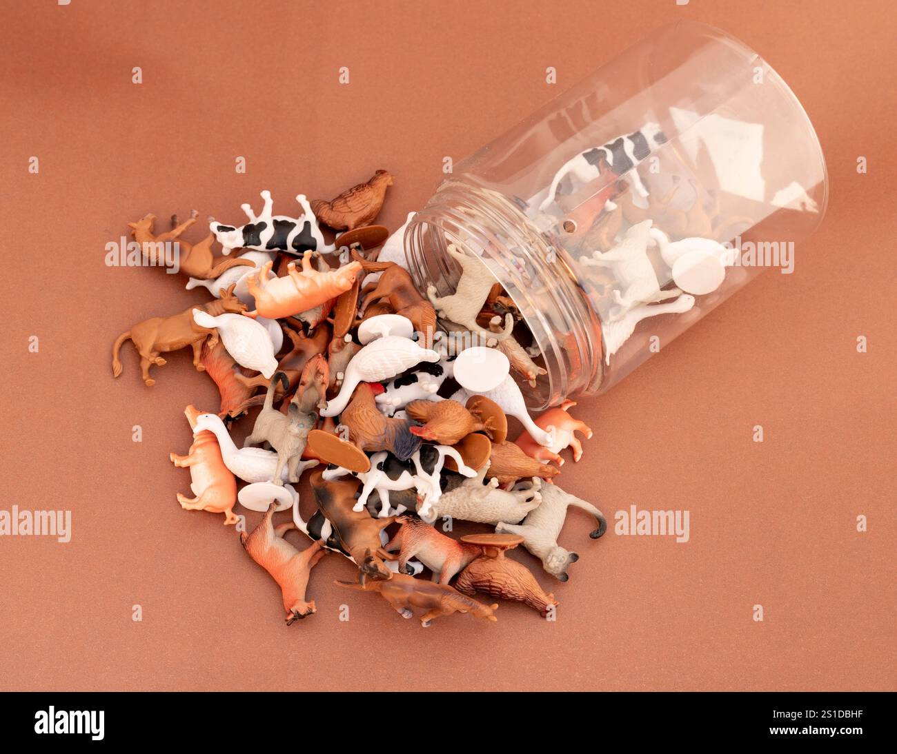 Figurines animales en plastique renversées d'un pot transparent sur fond brun Banque D'Images