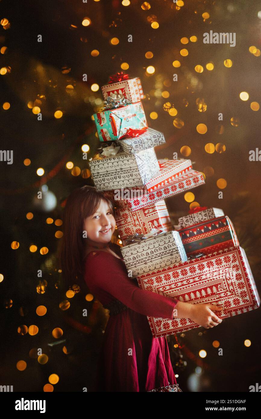 Fille tenant une pile de cadeaux debout devant des lumières scintillantes Banque D'Images