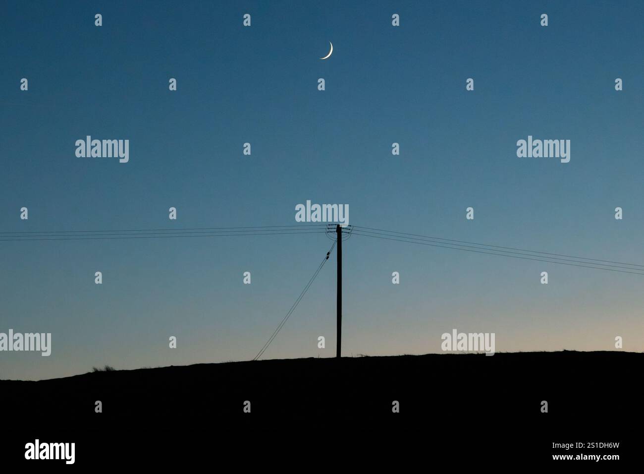 Poteau électrique et lignes électriques avec une nouvelle lune, vu contre un ciel nocturne clair Banque D'Images