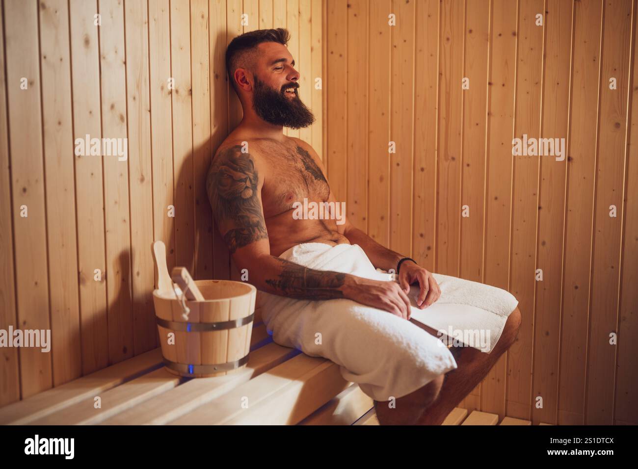 Un homme adulte se détend au sauna. L'homme barbu est assis dans le sauna et profite d'un traitement sain. Banque D'Images