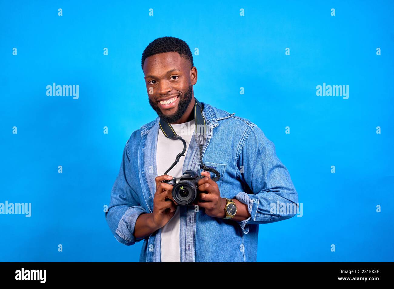 Jeune photographe souriant avec un appareil photo numérique dans un studio. Il est heureux et professionnel, montrant sa passion pour la photographie. Il se démarque à nouveau Banque D'Images