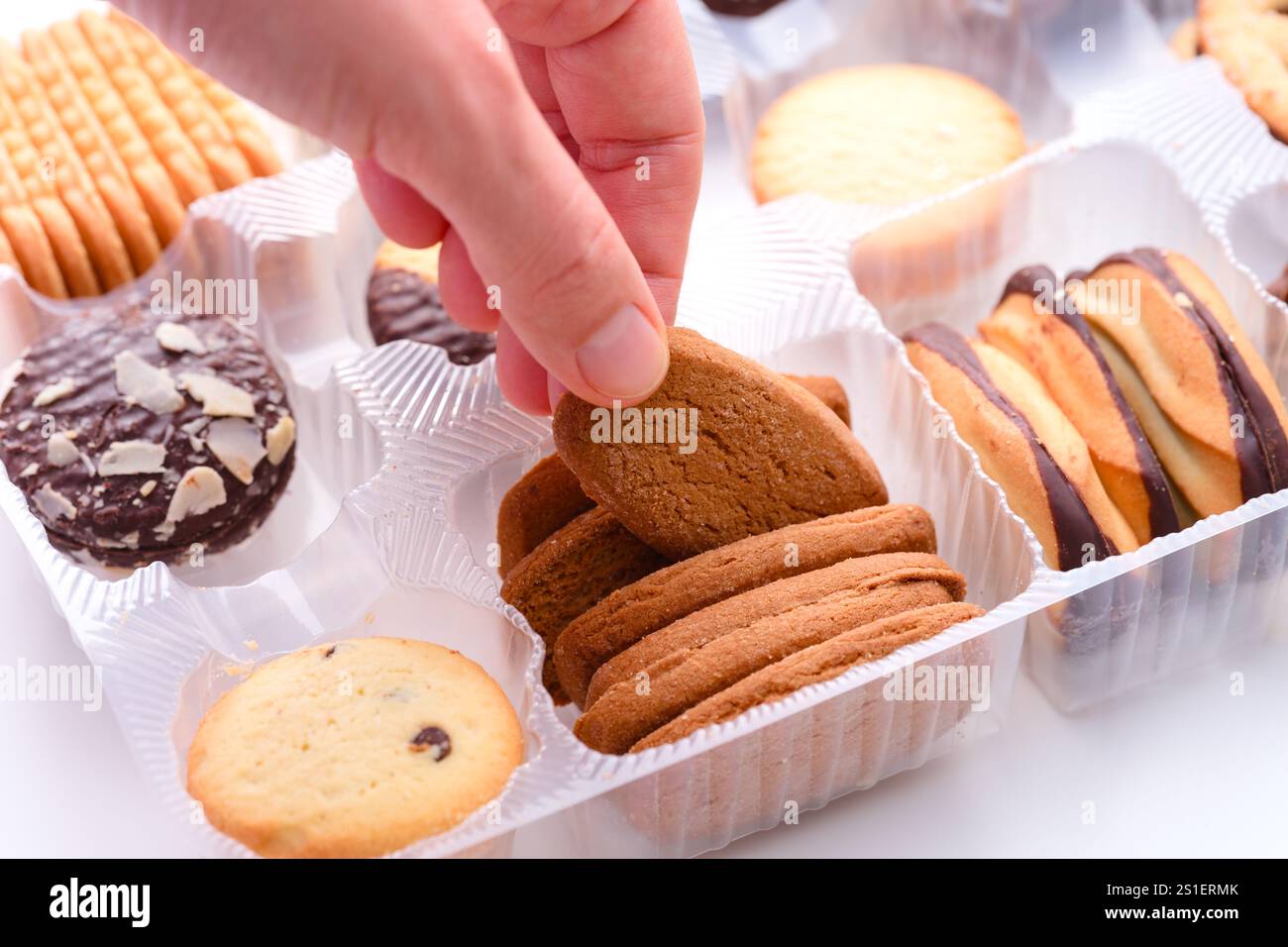 Main de femme prenant le cookie de la boîte en plastique avec différents types de cookies en elle. Gros plan Banque D'Images