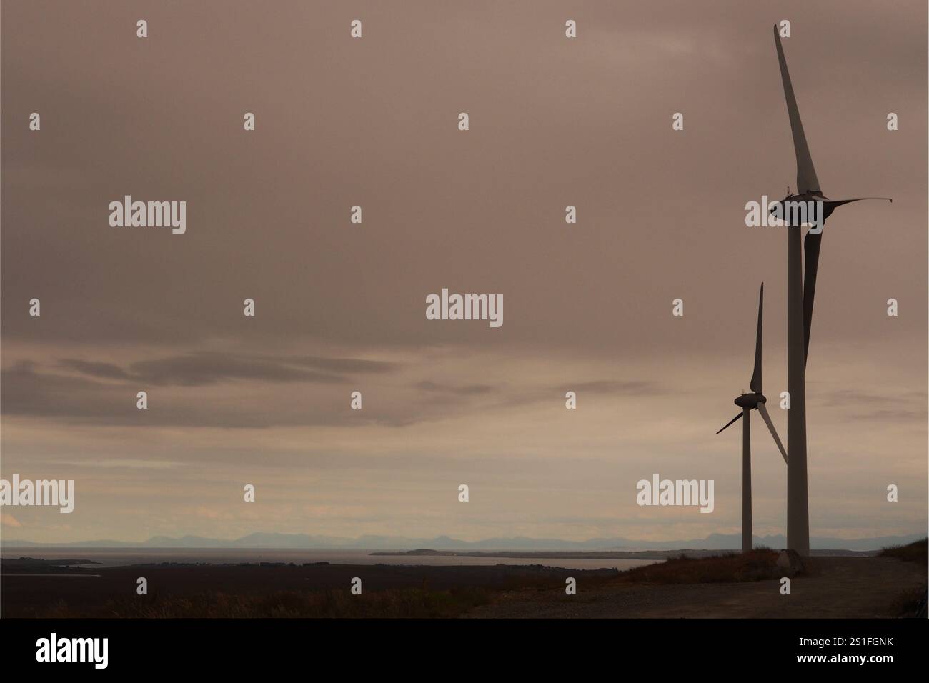 La silhouette de deux éoliennes à axe horizontal très haut contre un ciel nuageux et orageux sur l'île de Lewis, en Écosse, au Royaume-Uni, haut sur une colline. Banque D'Images
