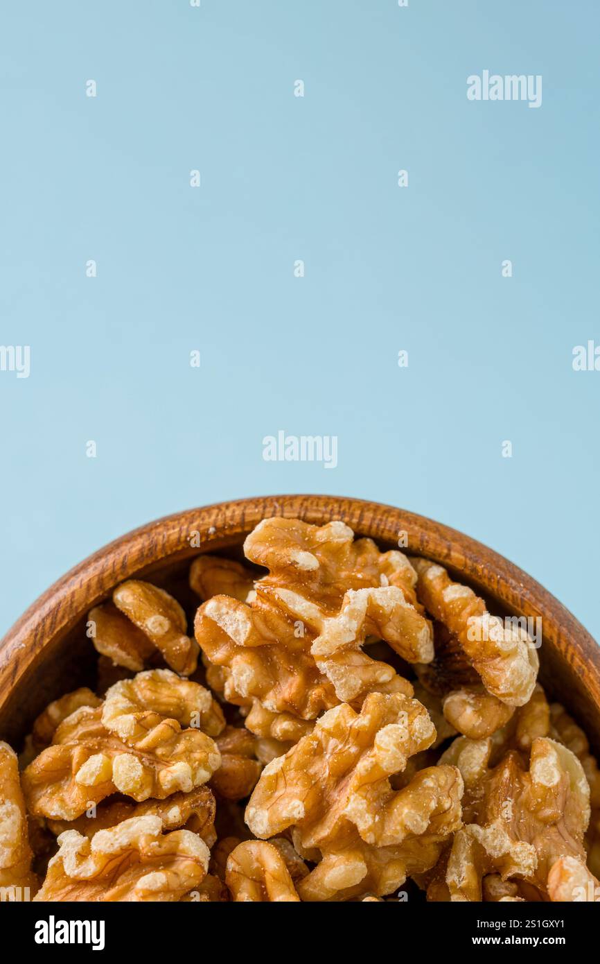 Vue de dessus d'un tas de cerneaux de noix dans un bol en bois sur fond bleu Banque D'Images