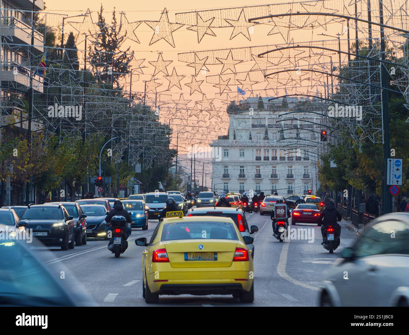 Athènes, Grèce - 3 janvier 2025 : route urbaine animée avec circulation sous des arches de décorations d'étoiles illuminées au crépuscule Banque D'Images