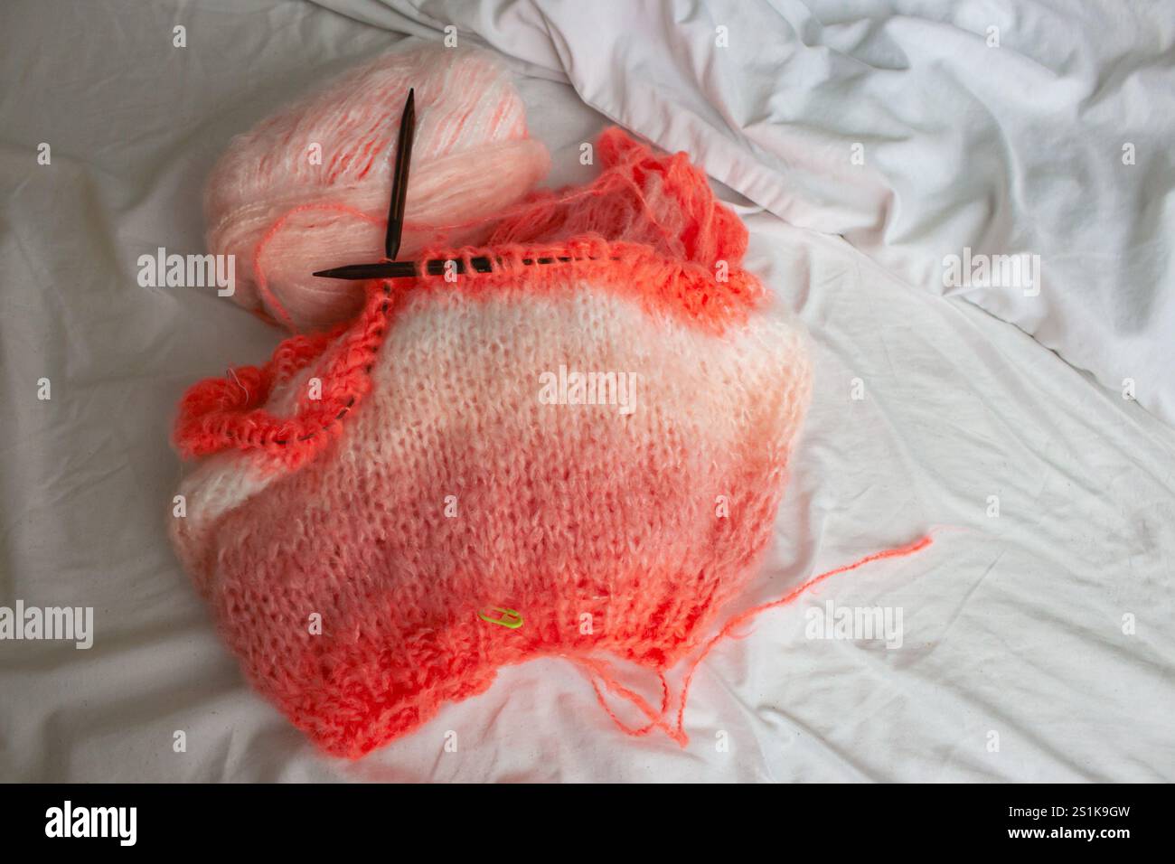 Motif de tricot corail et aiguilles à tricoter en bois sur drap de lit blanc, vue de dessus. Pull tricoté brillant avec boule de fil. Passe-temps de tricot Banque D'Images