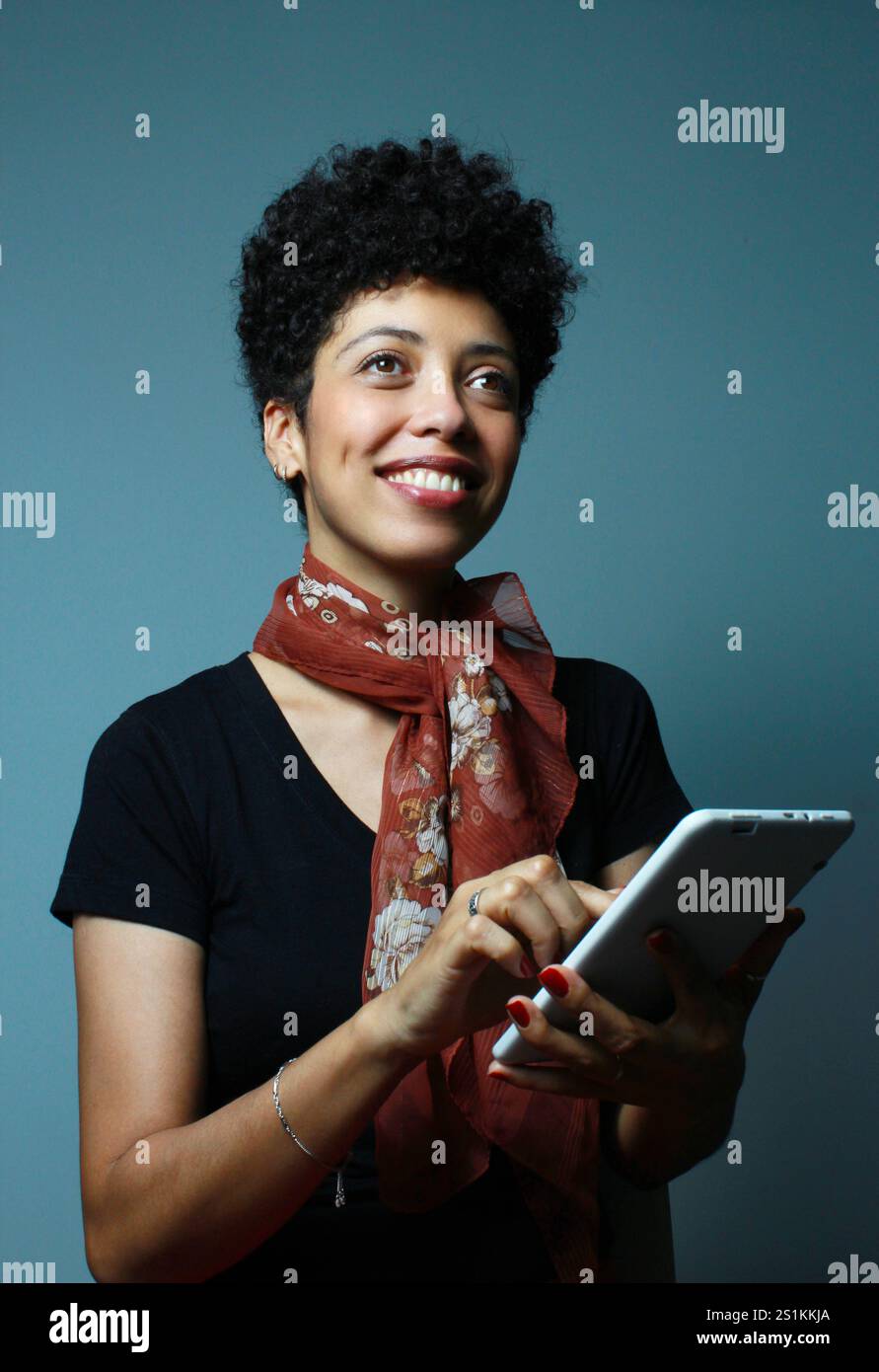 Femme joyeuse peau brune tenant une tablette sur ses mains et regardant vers le haut. Cours de collège, étudiant universitaire, hôtesse d'entreprise. Portrait vertical. Banque D'Images