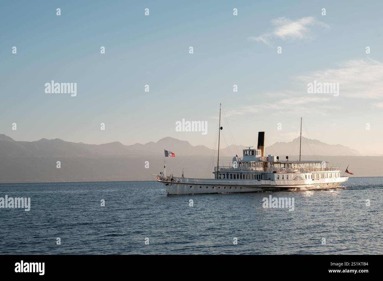 Bateau sur le lac Léman, Lausanne, et les Alpes en arrière-plan avec la lumière dorée du soleil sur le côté Banque D'Images