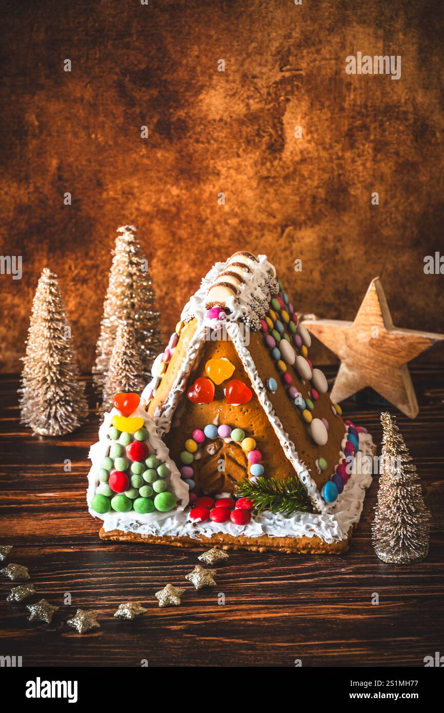 Maison en pain d'épice décorée de bonbons colorés et décoration de noël sur fond de bois, verticale avec espace copie Banque D'Images