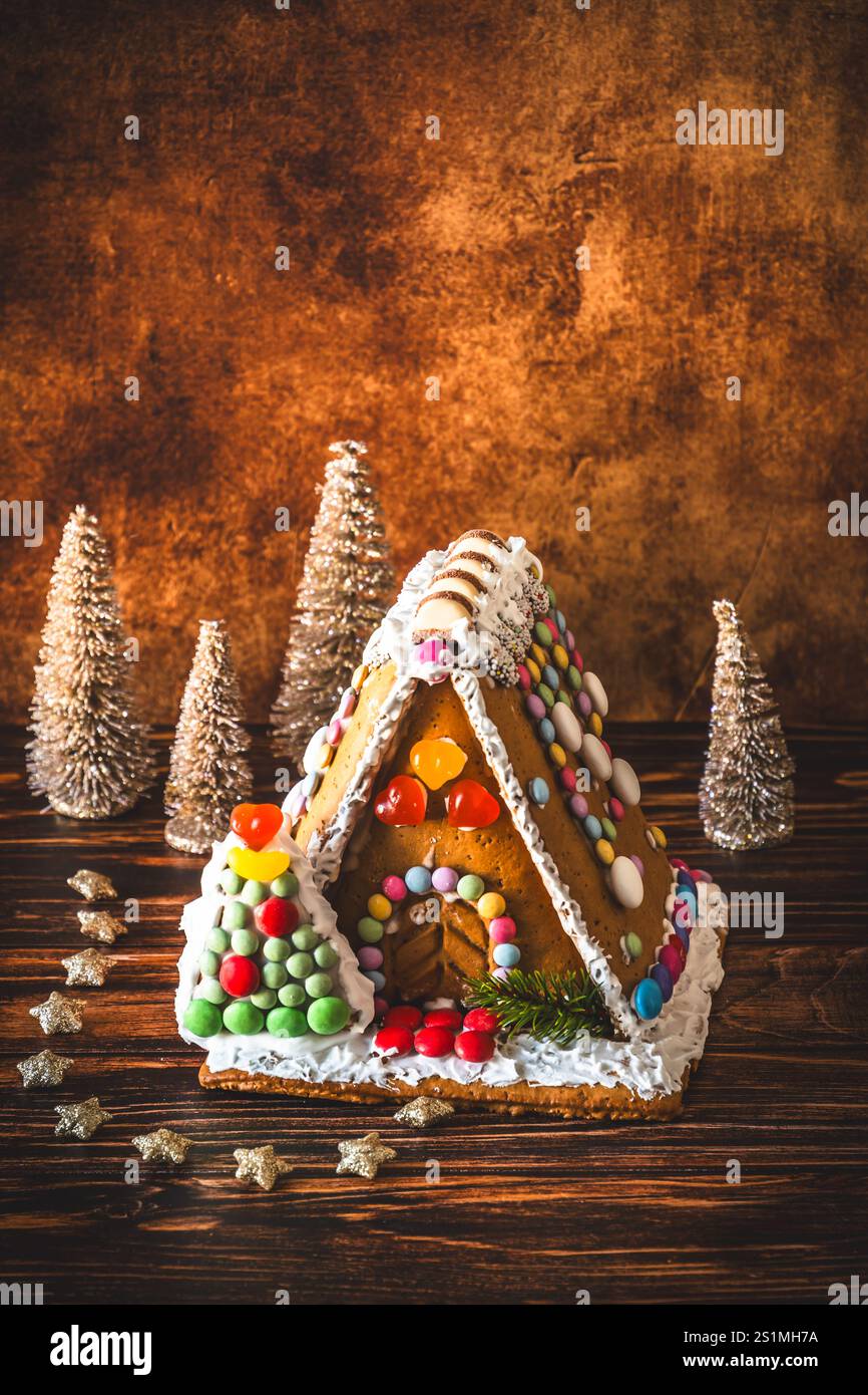 Maison en pain d'épice décorée de bonbons colorés et décoration de noël sur fond de bois, verticale avec espace copie Banque D'Images