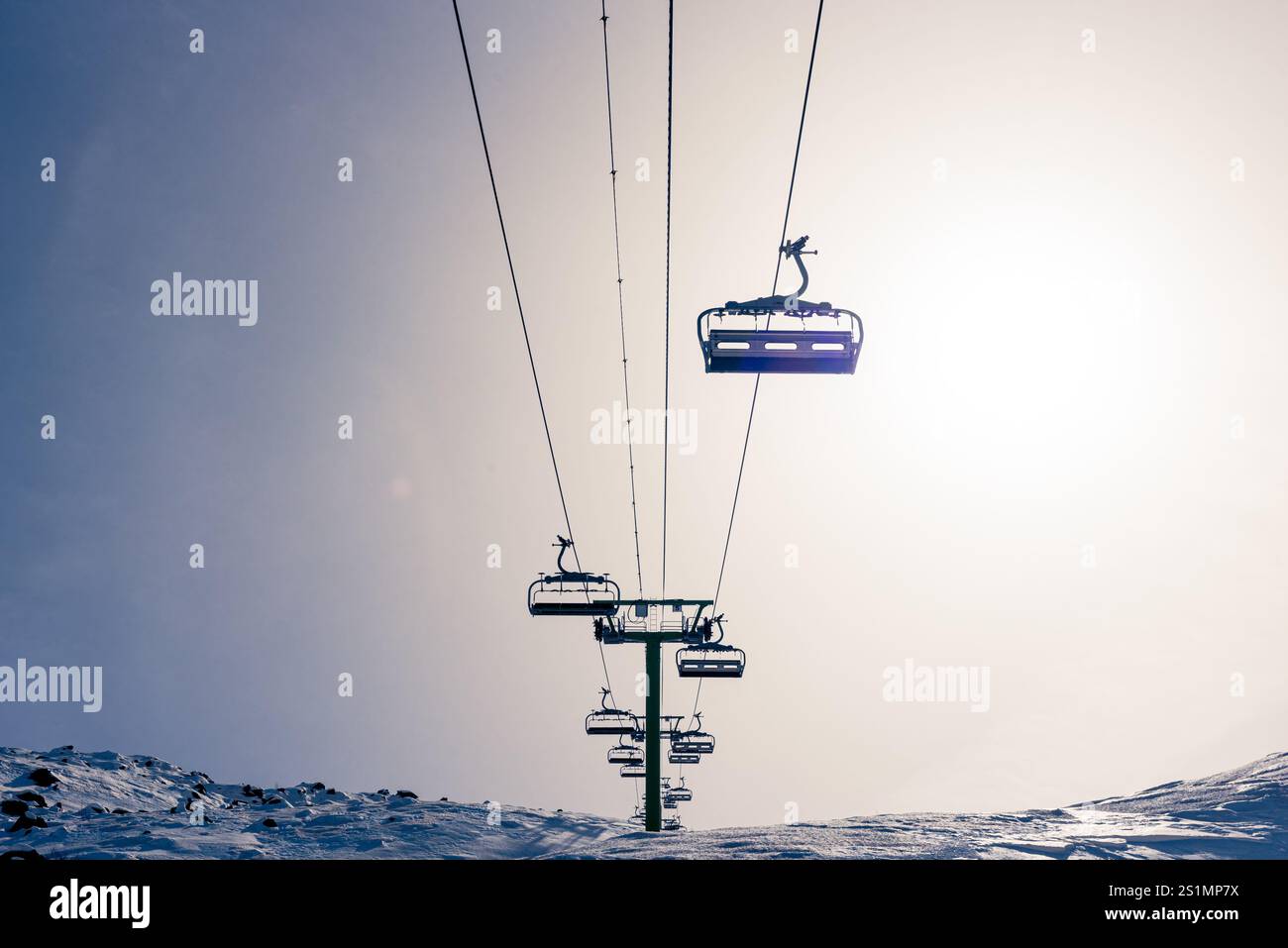 Ligne vide de télésièges face à la caméra, au sommet de la colline, contre-éclairée par le soleil Banque D'Images