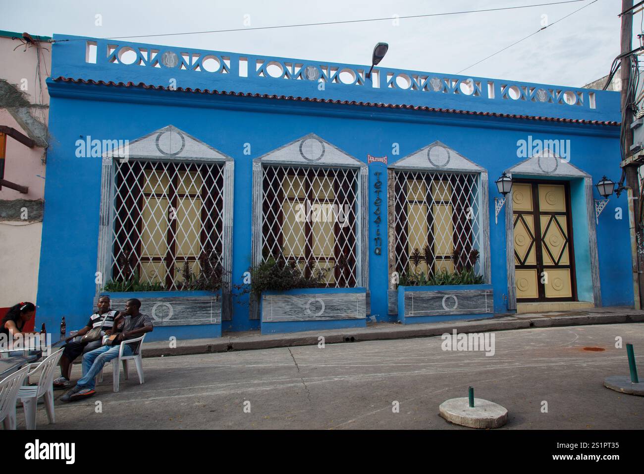 Les gens prenant une bière assis devant une façade bleue traditionnelle typique d'un bâtiment colonial sur la Plaza de Dolores, au centre-ville de Santiago de Cuba Banque D'Images