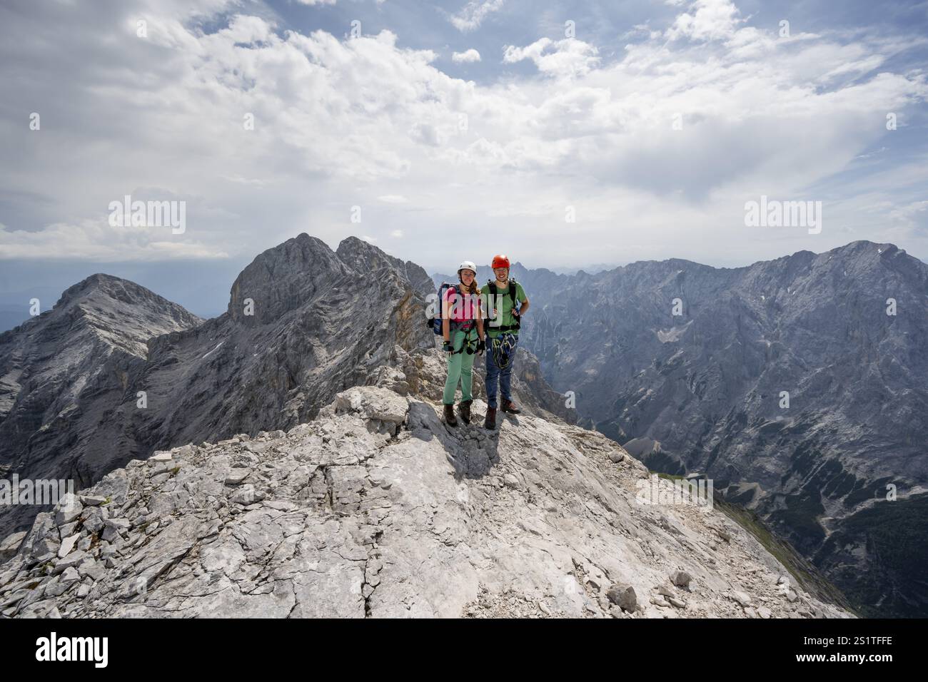 Couple, deux alpinistes avec des casques sur une étroite crête rocheuse, traversant le Jubilaeumsgrat, vue sur les sommets rocheux et Alpspitze, Wetterstein RA Banque D'Images