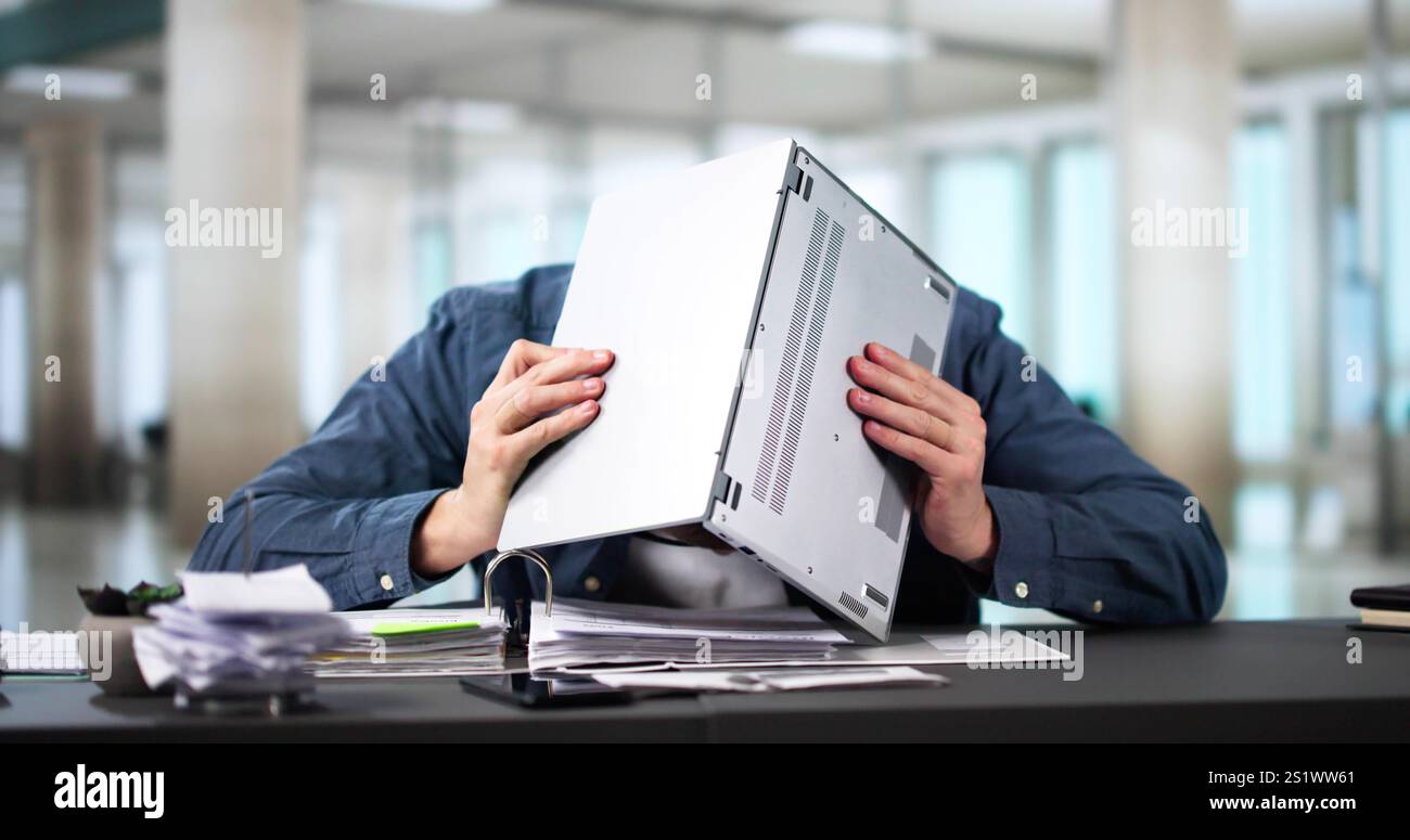 Jeune beau jeune homme d'affaires assis à son bureau derrière son ordinateur portable regardant la caméra Banque D'Images