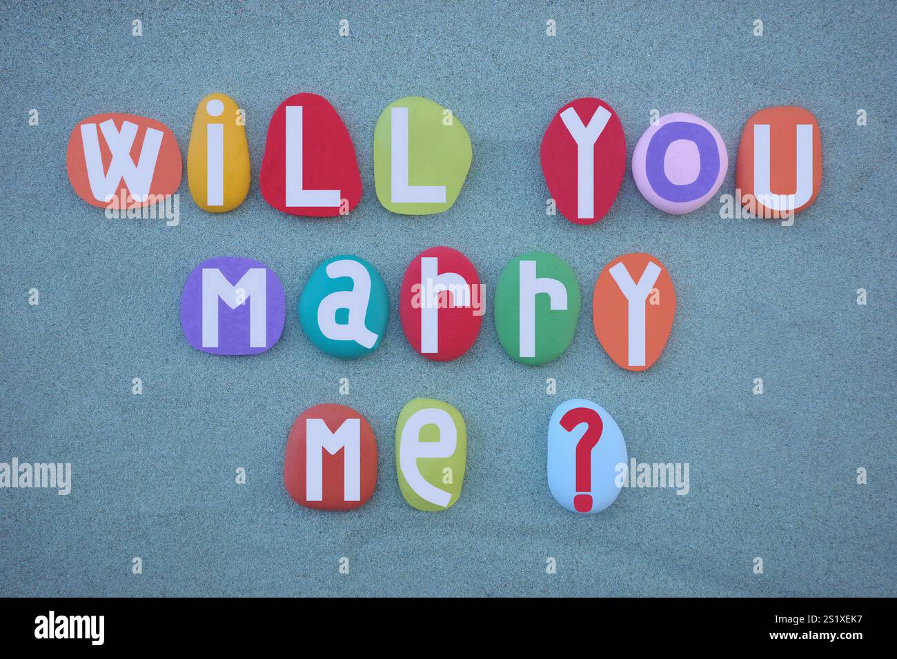 Voulez-vous me marier, message d'amour créatif composé de lettres en pierre peintes à la main multicolores sur sable vert Banque D'Images