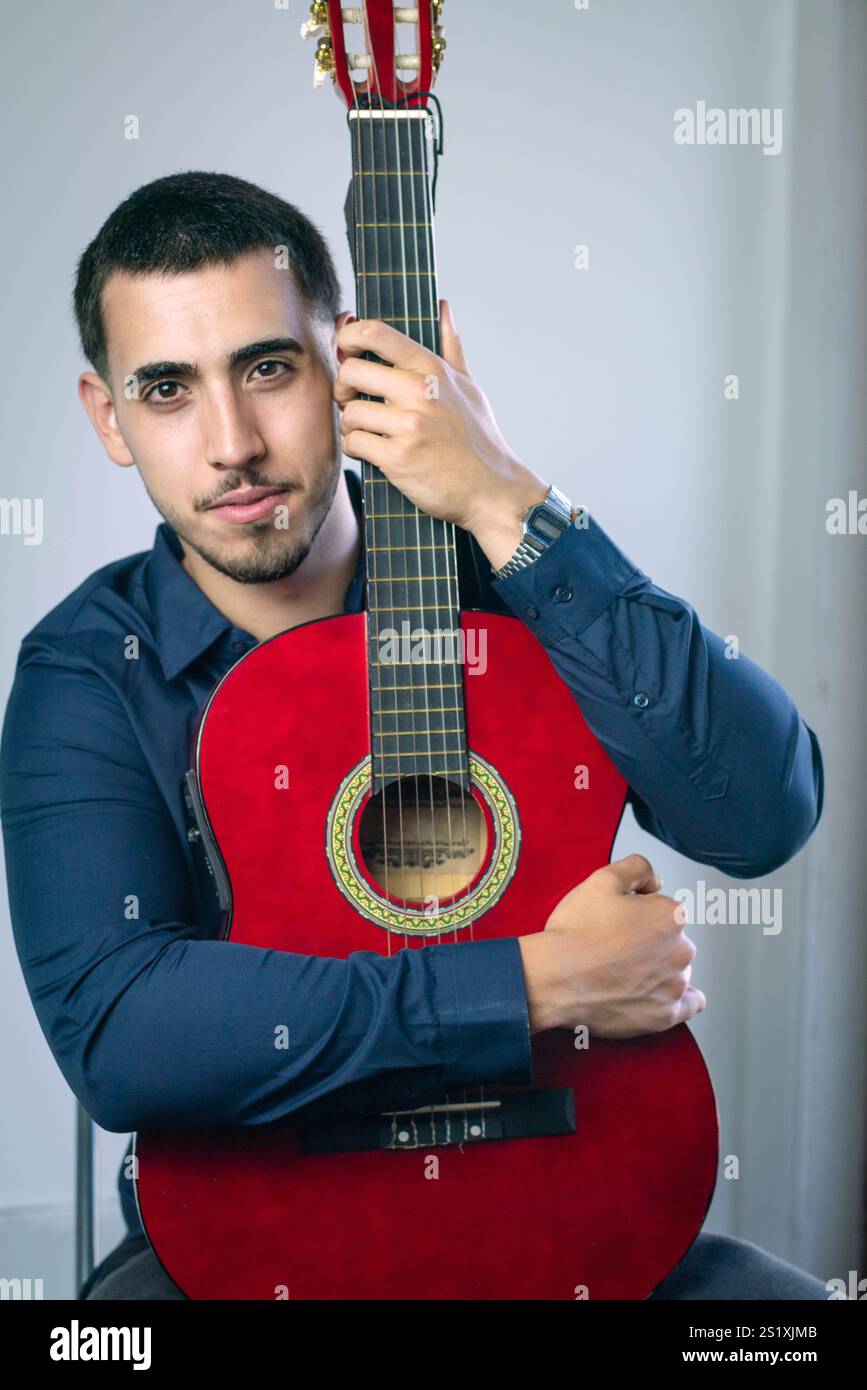 Jeune musicien embrassant tendrement sa guitare acoustique rouge, mettant en valeur son lien profond avec la musique. Banque D'Images