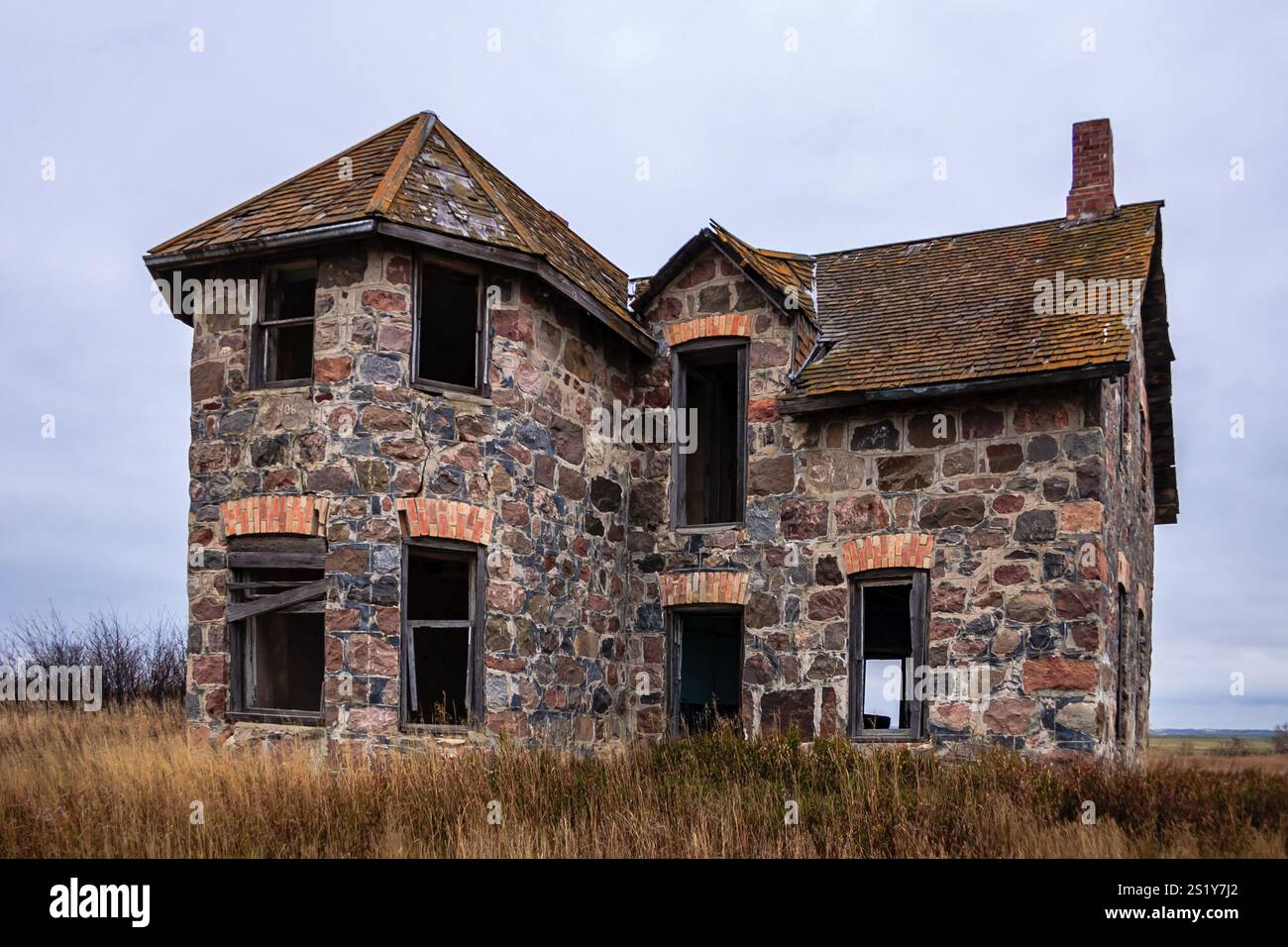 Une grande, vieille maison en pierre avec un toit incliné. La maison est vide et abandonnée. Le ciel est nuageux et l'herbe est sèche Banque D'Images