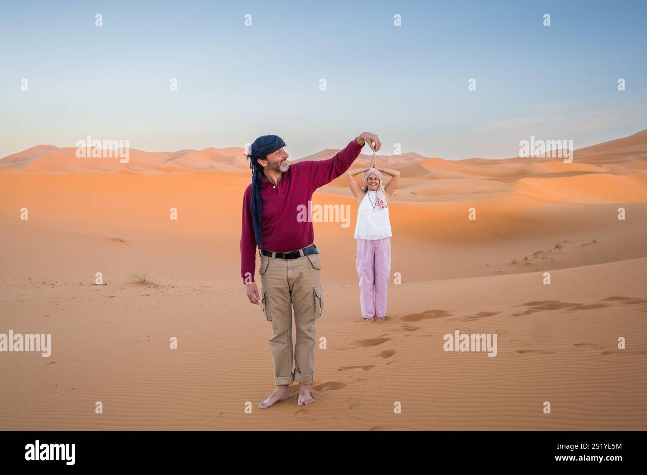 Un couple joue à faire des illusions d'optique au milieu du désert du Sahara. C'est le coucher du soleil dans le désert du Sahara à Merzouga, Maroc Banque D'Images