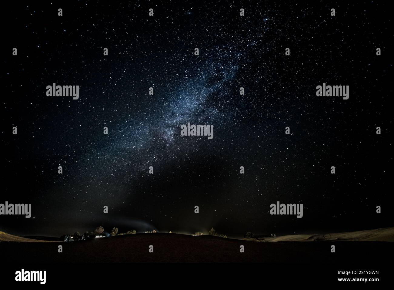 Superbe panorama nocturne dans le désert marocain. La voie lactée peut être vue très clairement. En arrière-plan, il y a un petit camp illuminé. Aventure Banque D'Images