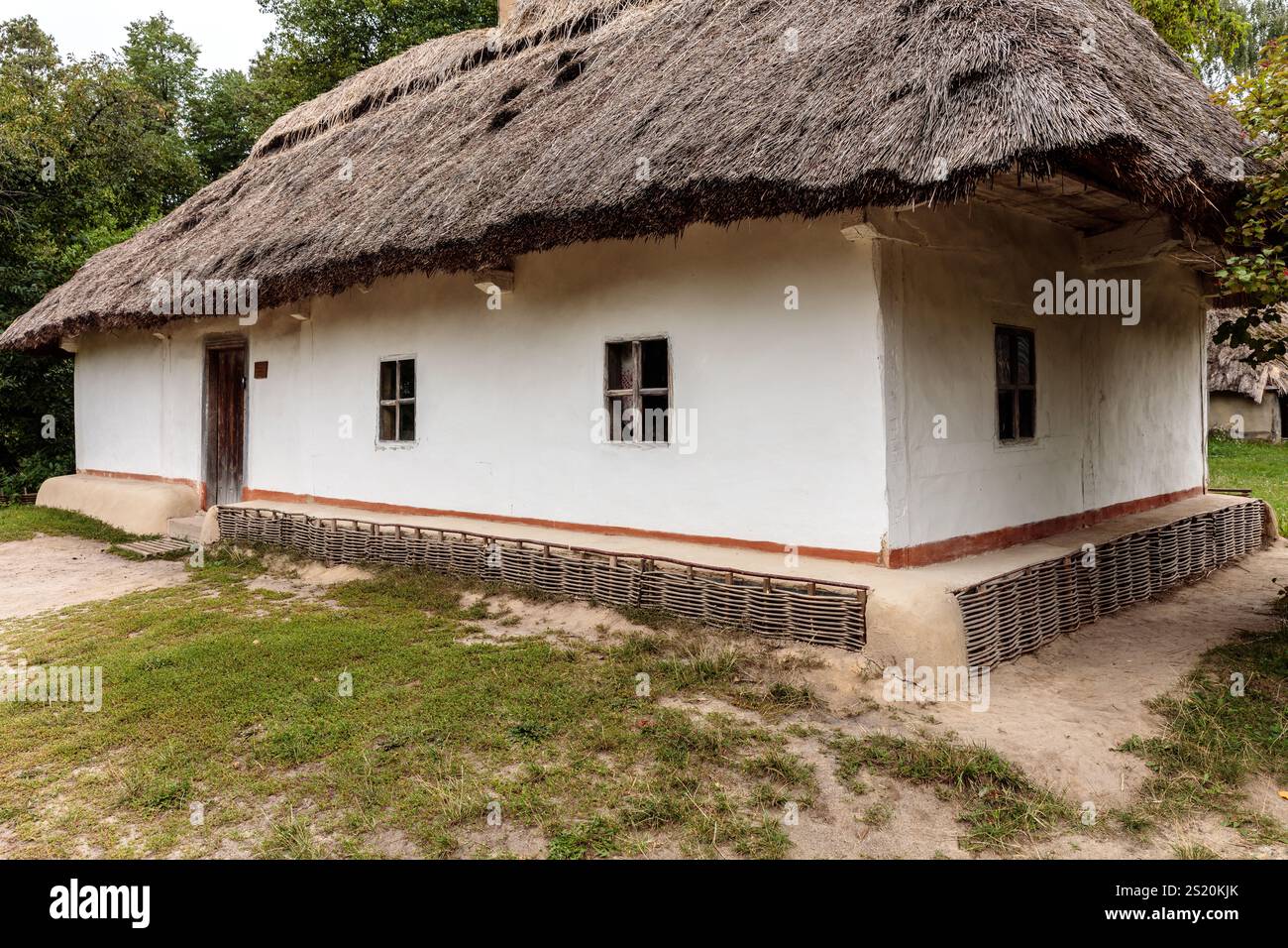 Une petite maison ancienne avec un toit de chaume et un extérieur blanc. La maison est entourée d'un champ de terre et a une fondation en pierre. La maison semble le faire Banque D'Images