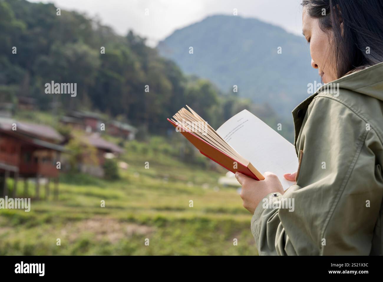 Une femme est assise dans la solitude tranquille lisant un livre entouré de feuilles vertes luxuriantes et vibrantes, incarnant la paix et la connaissance. Banque D'Images