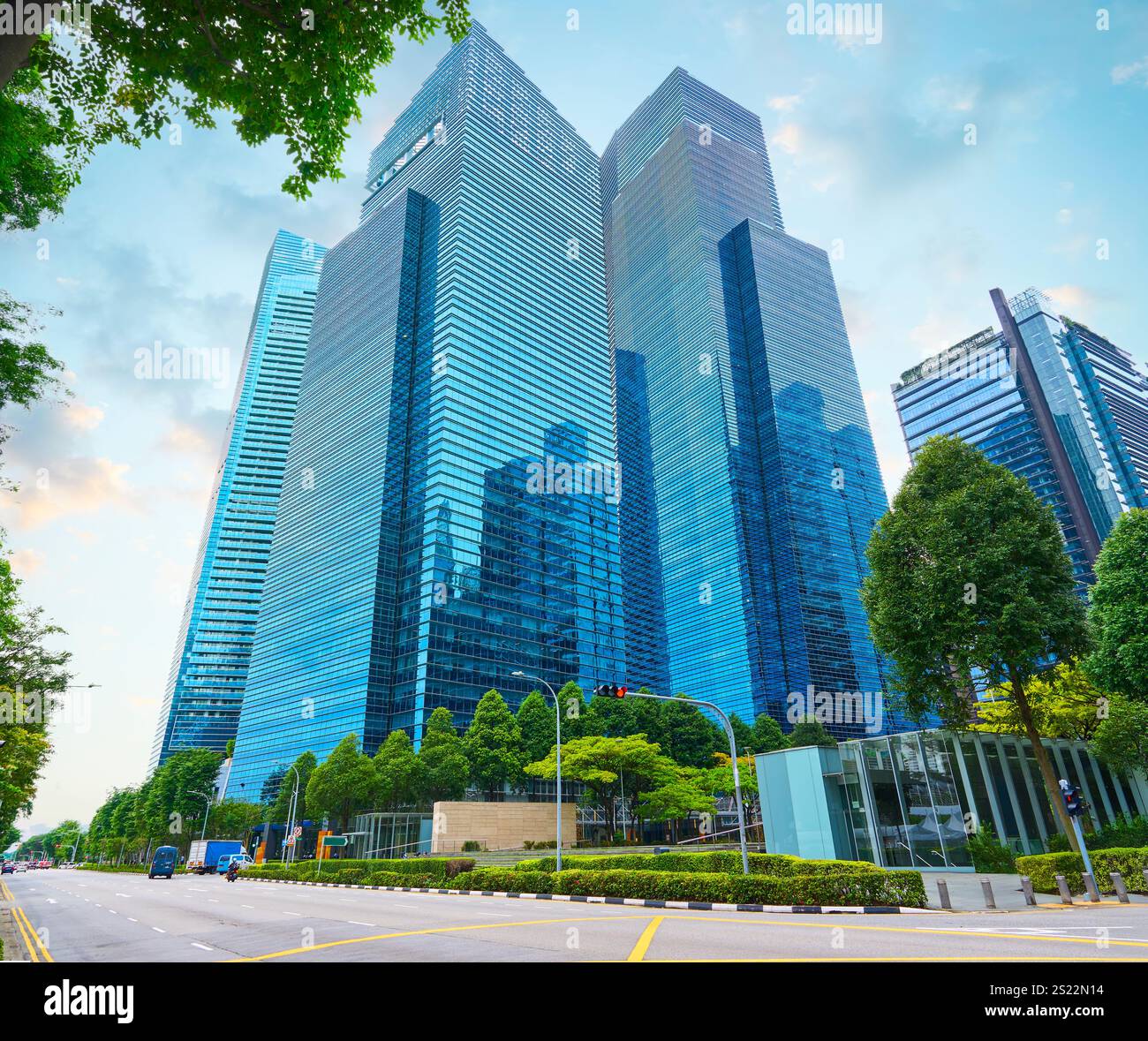 Gratte-ciel en verre s'élevant dans un quartier d'affaires urbain avec des arbres verts, mettant en valeur l'architecture moderne et le développement durable de la ville Banque D'Images