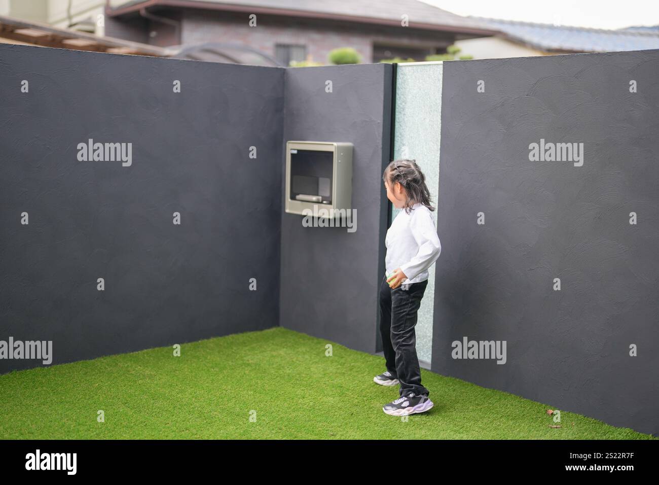 Un parent japonais et un enfant, un homme dans la vingtaine et une fille de 6 ans, jouent en se jetant des balles en plastique vert l'un sur l'autre dans le jardin clôturé de Banque D'Images