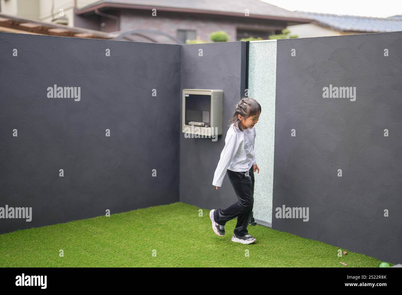 Un parent japonais et un enfant, un homme dans la vingtaine et une fille de 6 ans, jouent en se jetant des balles en plastique vert l'un sur l'autre dans le jardin clôturé de Banque D'Images