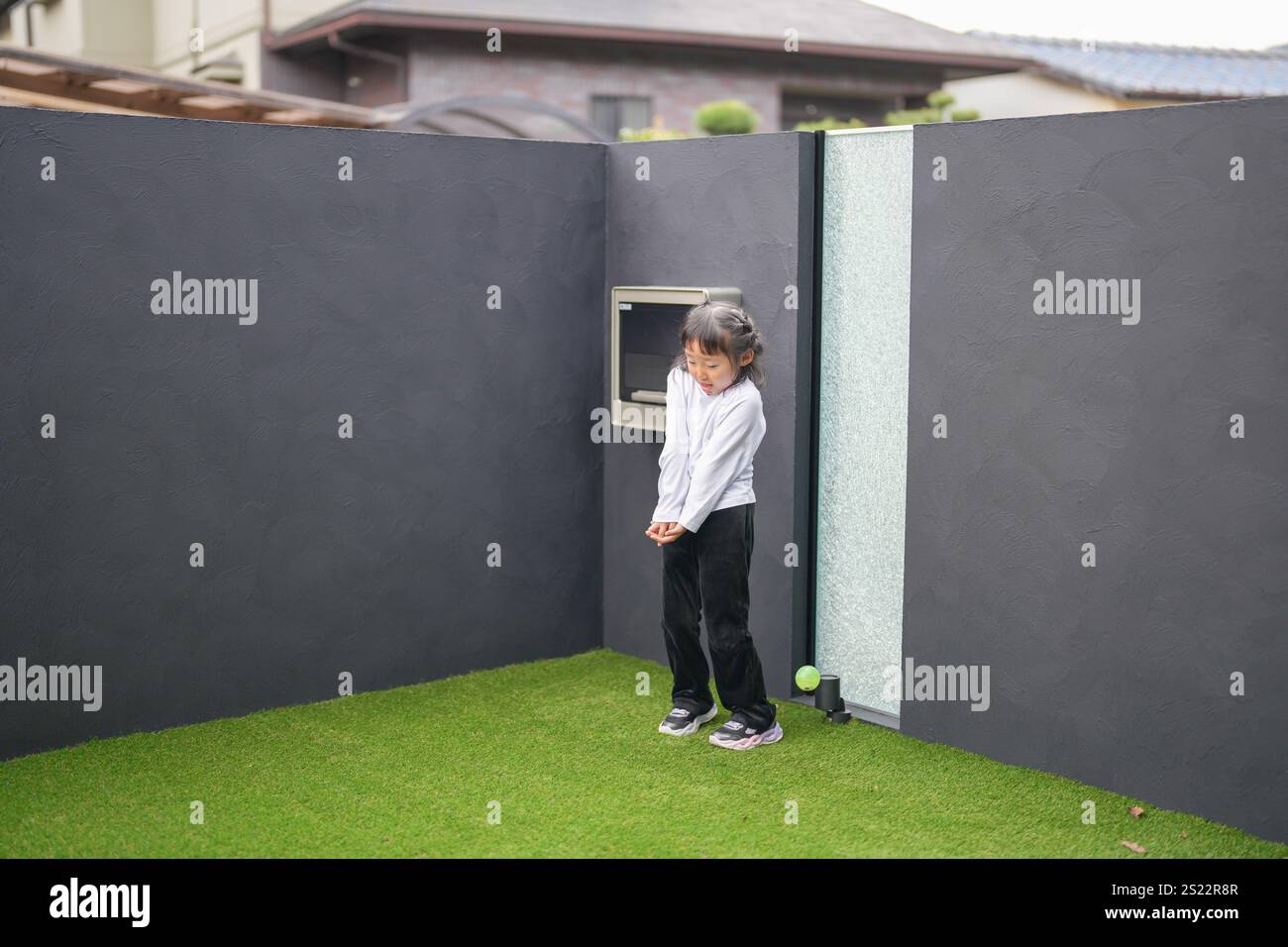 Un parent japonais et un enfant, un homme dans la vingtaine et une fille de 6 ans, jouent en se jetant des balles en plastique vert l'un sur l'autre dans le jardin clôturé de Banque D'Images