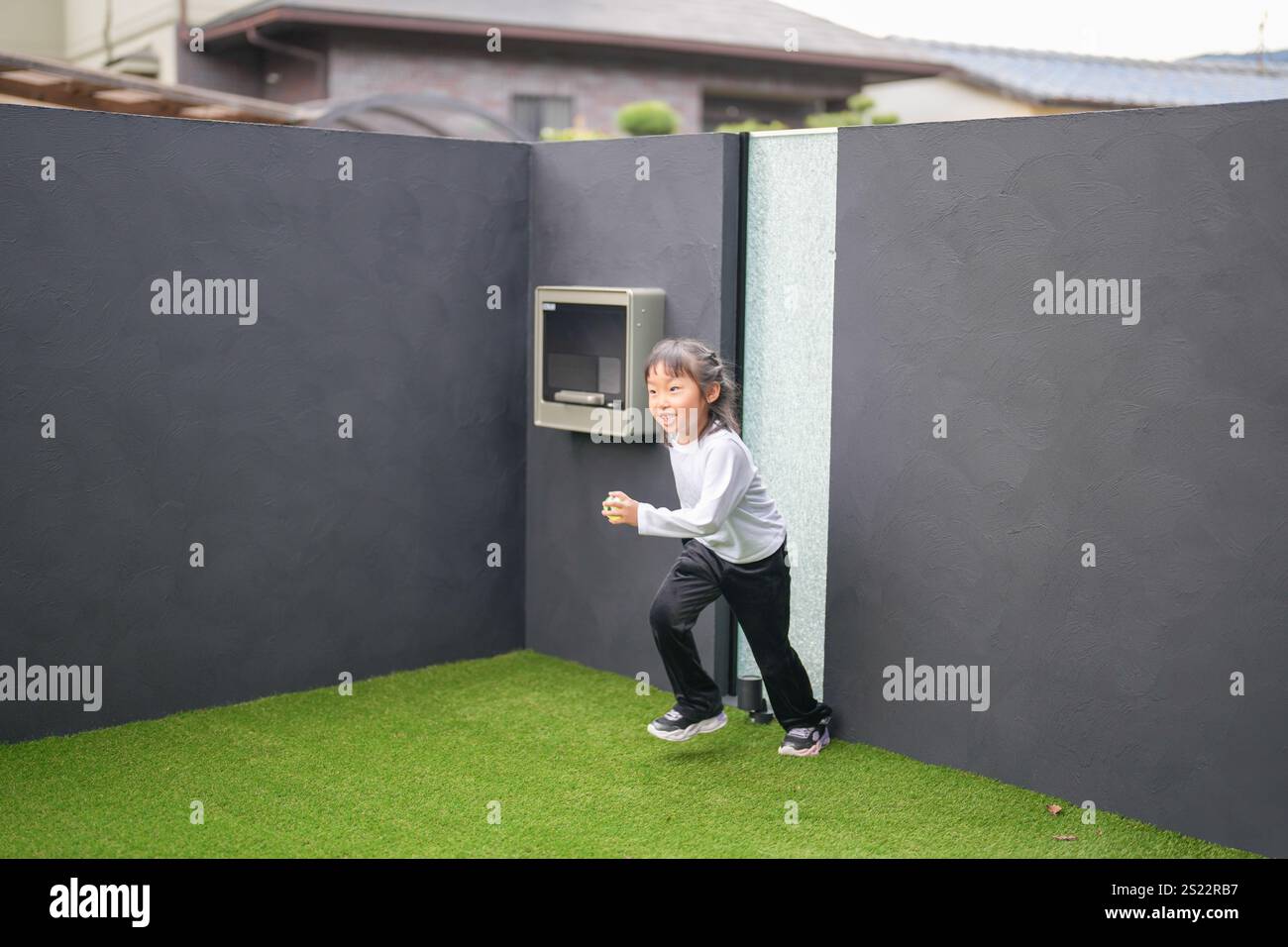 Un parent japonais et un enfant, un homme dans la vingtaine et une fille de 6 ans, jouent en se jetant des balles en plastique vert l'un sur l'autre dans le jardin clôturé de Banque D'Images