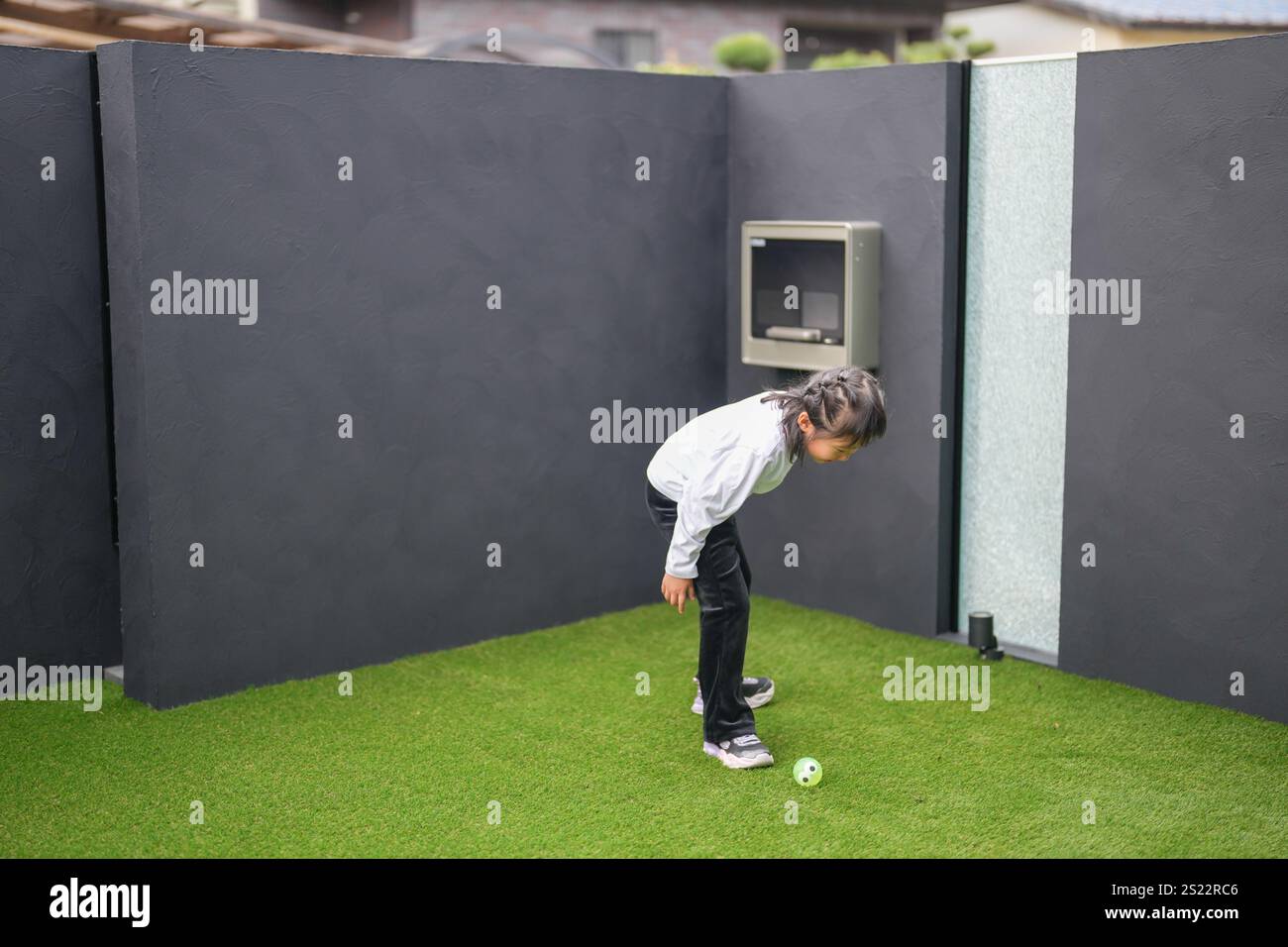 Un parent japonais et un enfant, un homme dans la vingtaine et une fille de 6 ans, jouent en se jetant des balles en plastique vert l'un sur l'autre dans le jardin clôturé de Banque D'Images