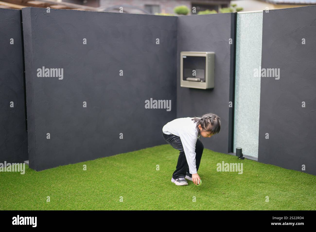 Un parent japonais et un enfant, un homme dans la vingtaine et une fille de 6 ans, jouent en se jetant des balles en plastique vert l'un sur l'autre dans le jardin clôturé de Banque D'Images