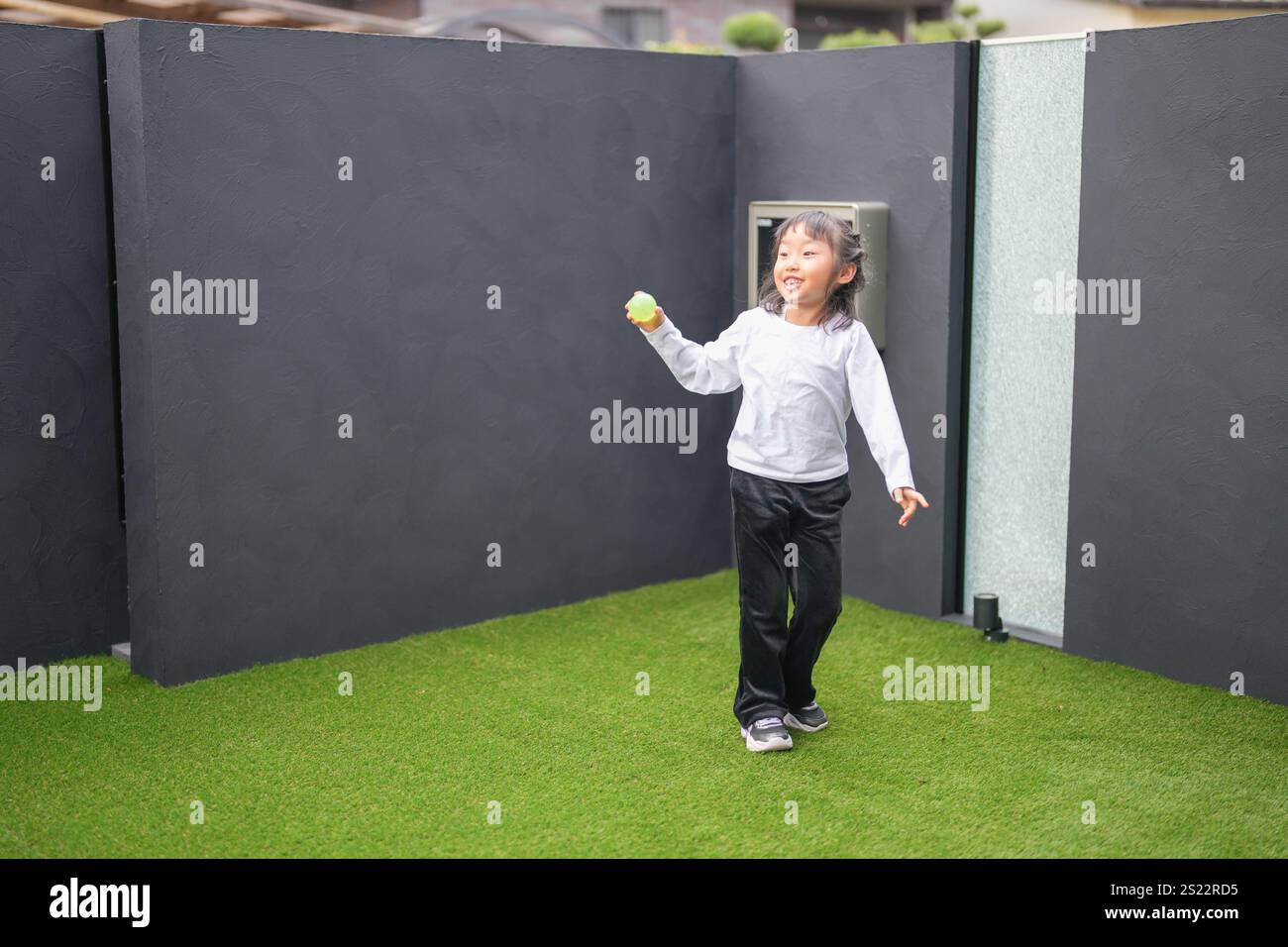 Un parent japonais et un enfant, un homme dans la vingtaine et une fille de 6 ans, jouent en se jetant des balles en plastique vert l'un sur l'autre dans le jardin clôturé de Banque D'Images