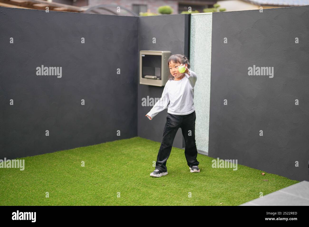 Un parent japonais et un enfant, un homme dans la vingtaine et une fille de 6 ans, jouent en se jetant des balles en plastique vert l'un sur l'autre dans le jardin clôturé de Banque D'Images