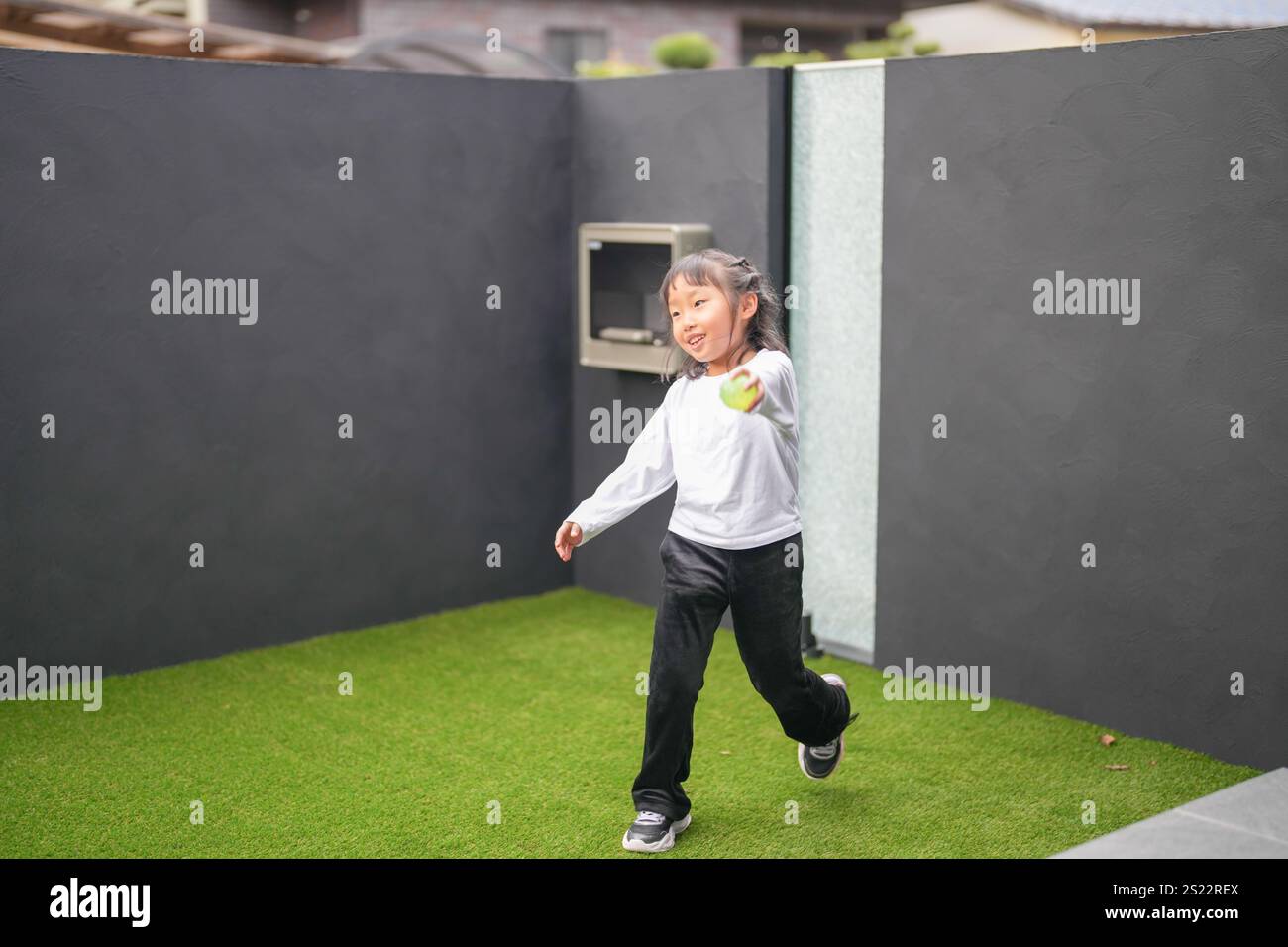 Un parent japonais et un enfant, un homme dans la vingtaine et une fille de 6 ans, jouent en se jetant des balles en plastique vert l'un sur l'autre dans le jardin clôturé de Banque D'Images