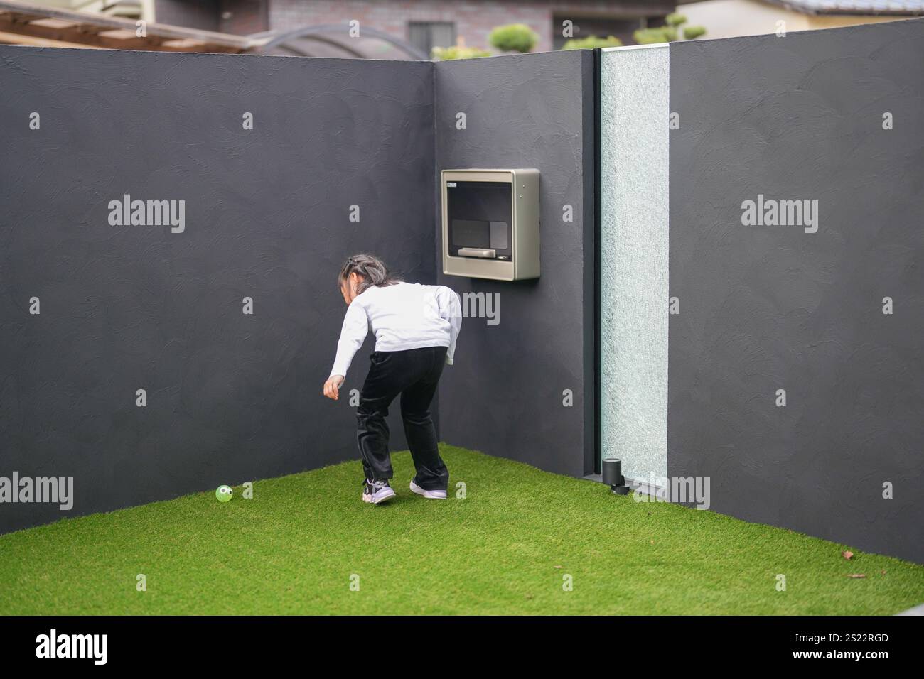 Un parent japonais et un enfant, un homme dans la vingtaine et une fille de 6 ans, jouent en se jetant des balles en plastique vert l'un sur l'autre dans le jardin clôturé de Banque D'Images