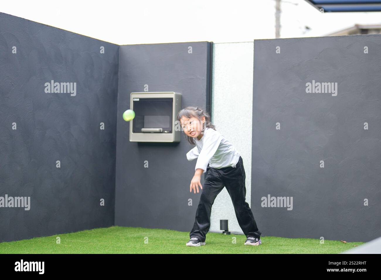 Un parent japonais et un enfant, un homme dans la vingtaine et une fille de 6 ans, jouent en se jetant des balles en plastique vert l'un sur l'autre dans le jardin clôturé de Banque D'Images